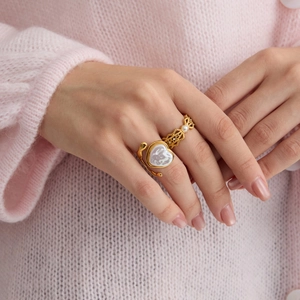 Détail de bague coeur en nacre et anneau perlé doré sur main et pull rose