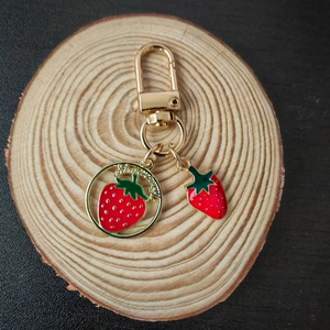 Detail view of golden strawberry keychain with enamel charm on round wooden base