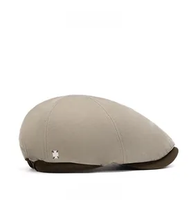 Detail view of khaki newsboy hat featuring brown corduroy brim and metal side emblem