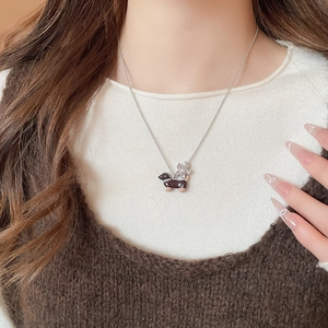 Détail des pendentifs teckel et fleur sur une chaîne en argent avec tricot douillet
