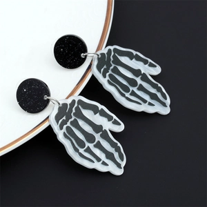 Gros plan de boucles d'oreilles main de squelette en acrylique noir et blanc d'Halloween