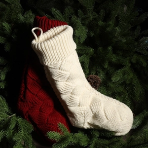 Close-up of red and cream knitted Christmas stockings with cable patterns on pine branches