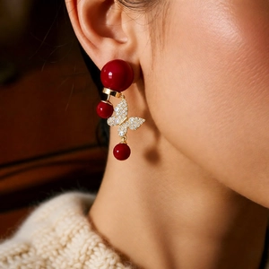Gros plan sur les boucles d'oreilles papillon dorées 18k avec perles rouges sur modèle