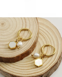 Detail of 18K gold-plated hexagonal earrings with pearls on a wooden display