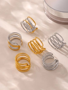 Close-up of stacked gold and silver multilayer open rings on a beige ripple surface