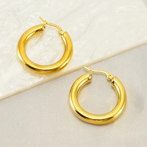 Détail des boucles d'oreilles créoles dorées polies sur fond de marbre minimaliste