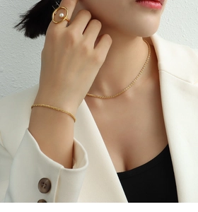 Close-up of gold chain necklace, bracelet and pearl ring set on model in white blazer