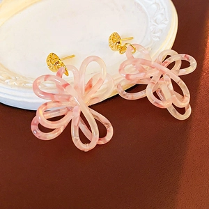 Dettaglio di orecchini a fiore in acrilico rosa marmorizzato con perni dorati su piatto