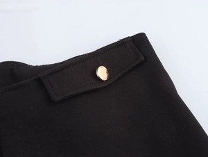 Detail of black low waist shorts featuring a metallic gold button on the side flap