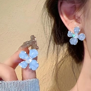 Close-up of light blue flower stud earrings with diamonds on a model's ear