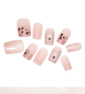 Detail view of pink ombre press-on nails with glitter and 3D butterfly charms