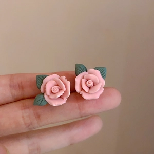 Dettaglio degli orecchini a rosa rosa con foglie verdi tenuti in mano per la dimensione