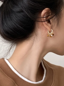 Détail de boucles d'oreilles pompon en œil de tigre et perle plaquées or 18 carats sur modèle