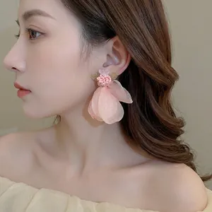 Pink tulle flower earrings with small beads and green leaves on a female model