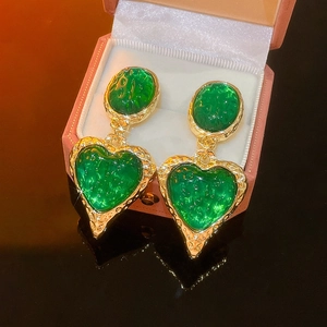 Dettaglio di orecchini vintage dorati con pietre verdi a cuore e texture screpolata
