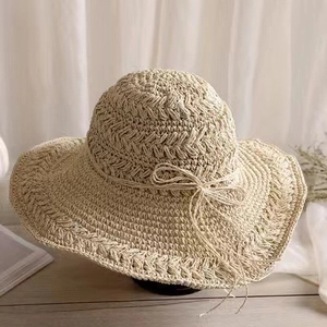 Chapeau de paille crocheté beige à large bord avec nœud élégant sur fond de bois clair