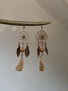 Détail de boucles d'oreilles attrape-rêves bohèmes avec feuilles de bronze et pompons