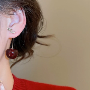 Dettaglio di orecchini a ciliegia in resina rosso scuro indossati con un maglione vintage