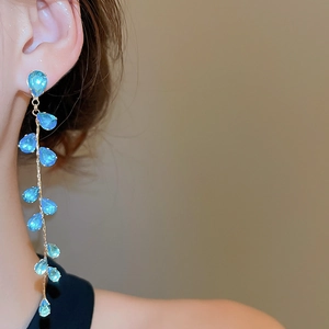 Macro shot of gold leaf tassel earrings with blue zircon waterdrop pendants on a model