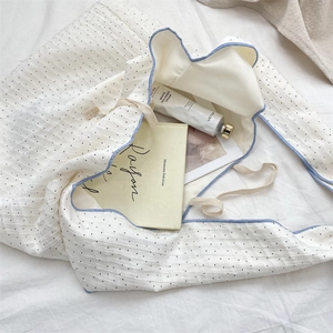Detail of white drawstring tote bag with black polka dots, blue piping and textured fabric