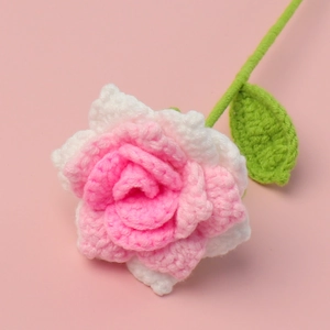 Handmade crochet rose flower in pink and white with green stem on pink background