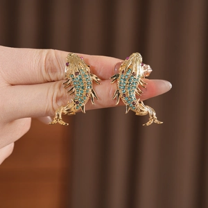 Detailed close-up of golden fish earrings with sparkling blue and green crystals
