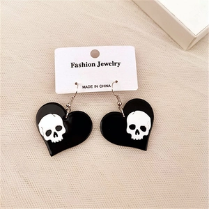 Detail of gothic heart-shaped earrings with white skull pattern on a woven background