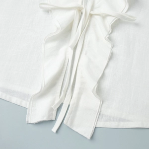 Detail shot of white cotton shirt set featuring ruffled edges and lace-up texture
