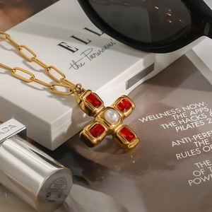 Collier croix doré avec gemmes rouges et perle sur fond de magazine de luxe
