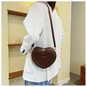 Borsa a tracolla marrone a forma di cuore indossata da modella in completo bianco elegante