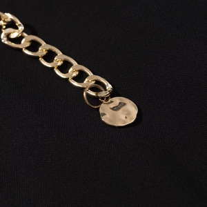 Dettaglio catena dorata spessa con ciondolo martellato su tessuto a maglia nera