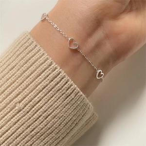 Detail of silver heart charm bracelet worn on wrist with cozy beige knit sweater background