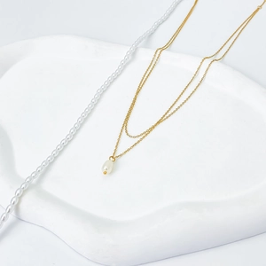 Detail of a double-layered gold necklace featuring a teardrop pearl on a white tray