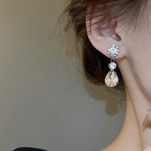 Close-up of sparkling flower and teardrop crystal earrings worn by a model