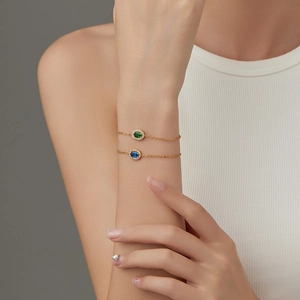 Close-up of gold chain bracelets with green and blue oval stones on a wrist