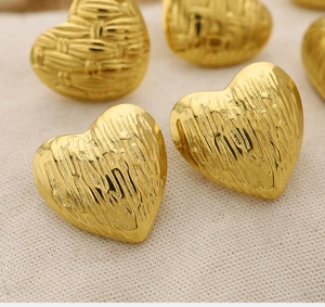 Macro shot of 18K gold heart earring with intricate woven texture on beige fabric