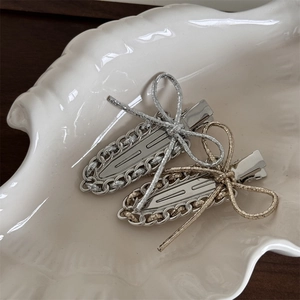 Detailed view of silver and gold metal chain hair clips with ribbon bow on a white plate