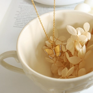 Elegant gold butterfly pendant necklace with zircon accents on a white relief cup