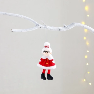 Plush Santa and Mrs. Claus ornaments hanging on snowy branches with festive lights