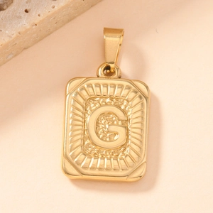 Macro detail of vintage gold square pendant with embossed letter G and hammered texture