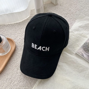 Detailed view of black cotton baseball cap with white BEACH embroidery on soft carpet