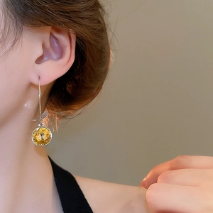 Close-up of sparkling yellow faceted gemstone earrings with elegant leaf-shaped silver hook
