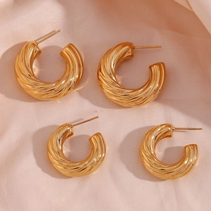 Detail of two pairs of gold hollow C-shape spiral earrings on soft pink silk fabric