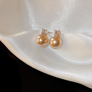 Vue macro des boucles d'oreilles perles plaquées or avec zircon sur soie blanche