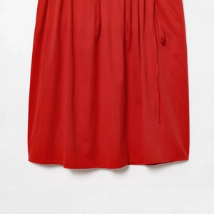 Robe midi rouge tendance avec nœud montrant la texture du tissu et l'ourlet drapé
