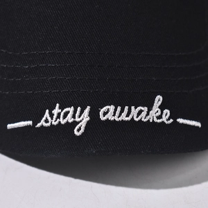 Detail der weißen Stay Awake Stickerei auf schwarzer Baumwollkappe mit Ziernähten