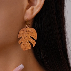 Macro detail of wood leaf drop earring featuring monstera leaf pattern and golden hook