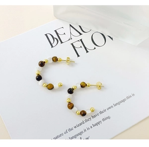 Detail of S925 silver C-shape earrings with tiger eye stones and golden metal beads