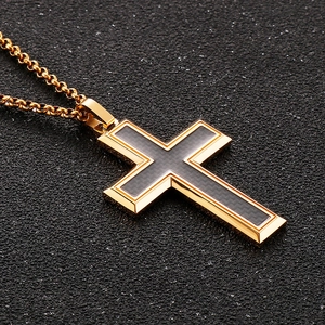 Close-up of gold titanium cross pendant with black resin inlay on textured surface