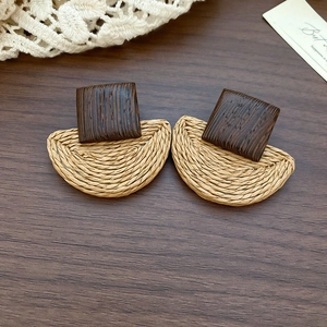 Detailed shot of wooden square stud and woven raffia fan pendant earring on wood background